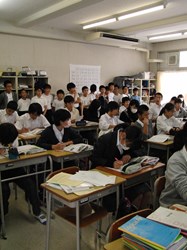 教室の後ろで授業を見る小学生と、背後に視線を感じている様子の中学生