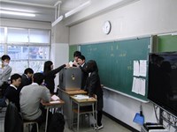 教室で、教卓におかれた投票箱に投票する生徒の写真