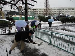 雪かきをする職員と登校する子どもたち