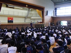 体育館で実行委員長の話を聞く生徒たち