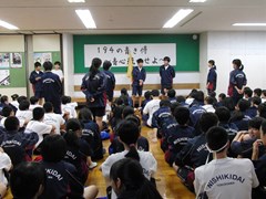 体育館で実行委員長の話を聞く生徒たち