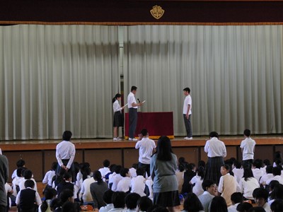 体育館ステージ上で委嘱状が手渡されるようす