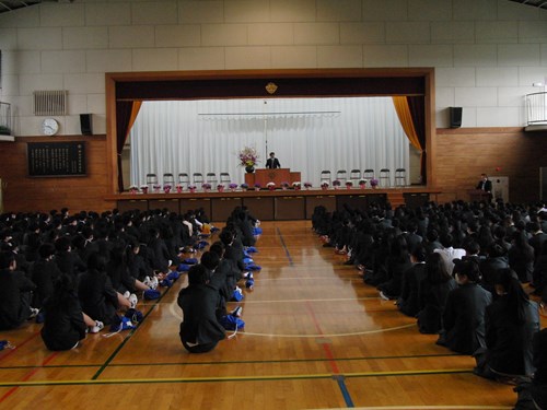 壇上の校長先生の話を座って聞く生徒