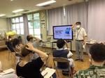 前半講義の様子。「百会（ひゃくえ）」というツボを押す講師と参加者たちの写真。※百会穴は左右の耳の一番高いところを頭の上で結んだ場所にあります。