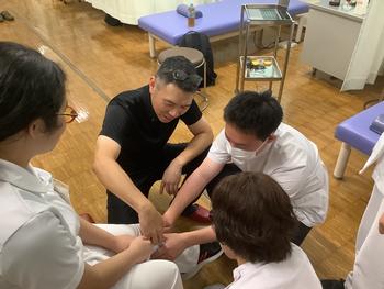 写真1は、3年生が近藤先生に膝関節の触察を教えて頂いている写真です。 写真1は、3年生が近藤先生に膝関節の触察を教えて頂いている写真です。