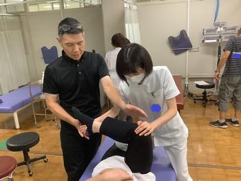 写真2は、生徒が近藤先生に教えて頂きながら股関節のストレッチングを行っている写真です。 写真2は、生徒が近藤先生に教えて頂きながら股関節のストレッチングを行っている写真です。